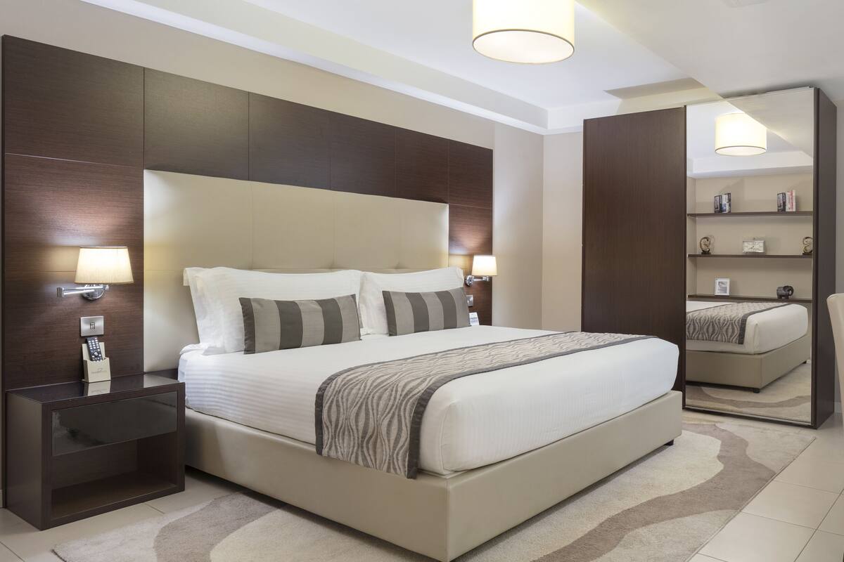 Une chambre d’hôtel moderne avec un grand lit, des tables de chevet, un bureau avec une lampe et un miroir.