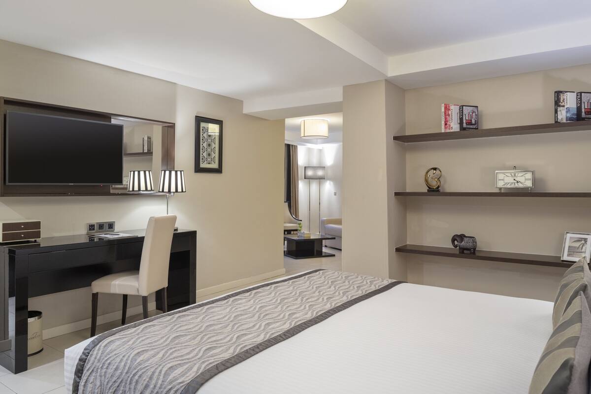Une chambre d’hôtel équipée d’un lit, d’un bureau, d’une chaise, d’une télévision et d’étagères contenant des livres et des objets décoratifs.