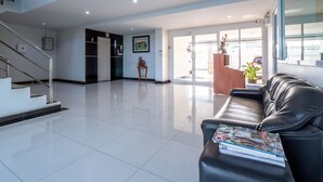 A modern lobby with a reception desk, a staircase, and a waiting area with a leather couch. - Taweesuk Residence (Samut Sakhon)