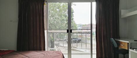 Habitación de hotel con cama, escritorio, aire acondicionado y puerta corrediza de vidrio que da a un balcón.