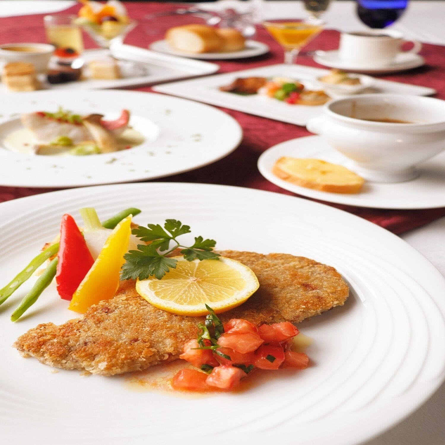 A plated dish with a breaded cutlet, lemon slice, parsley, and tomato garnish.
