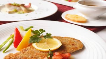 A plated dish with a breaded cutlet, lemon slice, parsley, and tomato garnish.