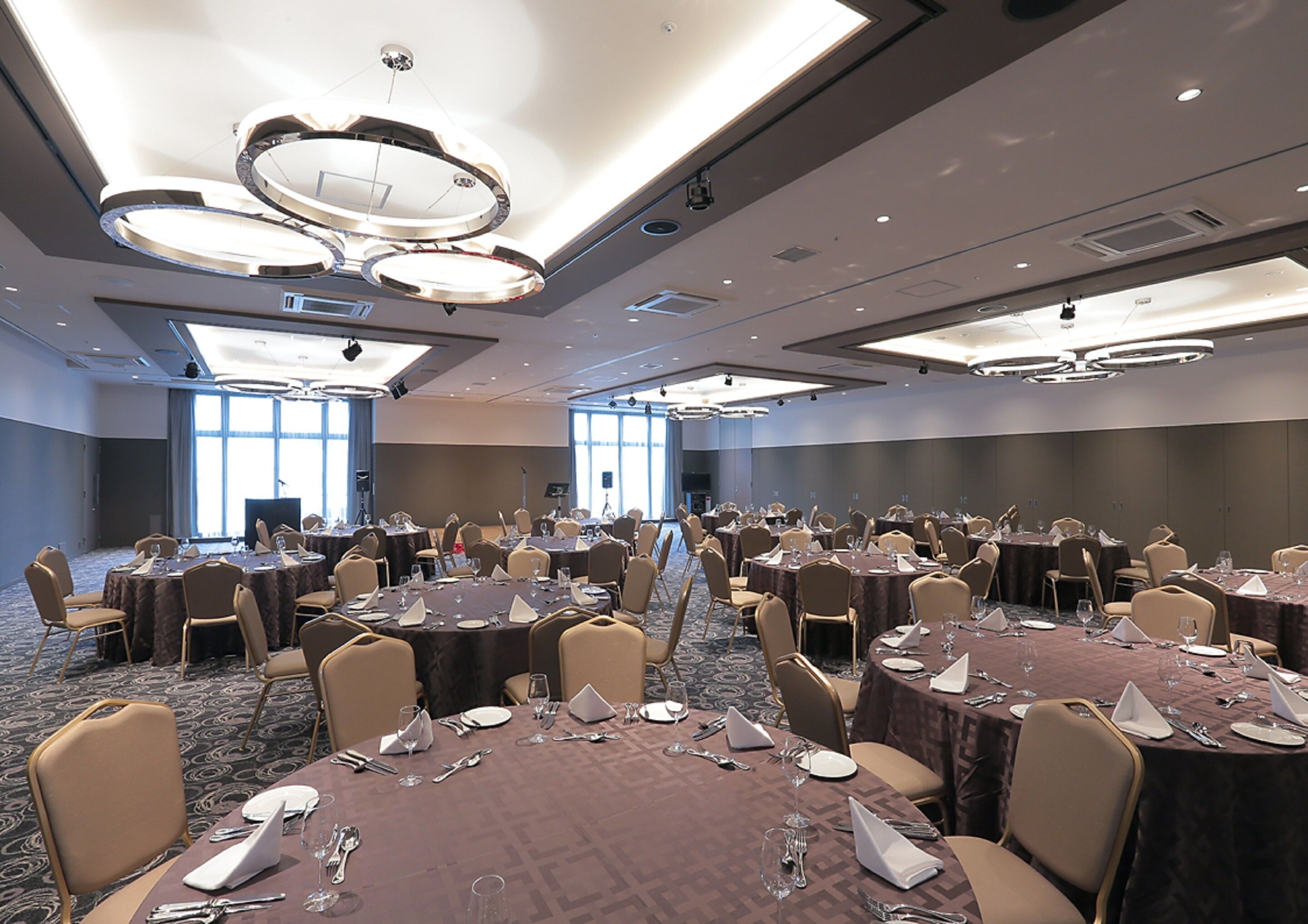 Un salón de conferencias con varias mesas redondas, cada una dispuesta con sillas y lo necesario para comer.