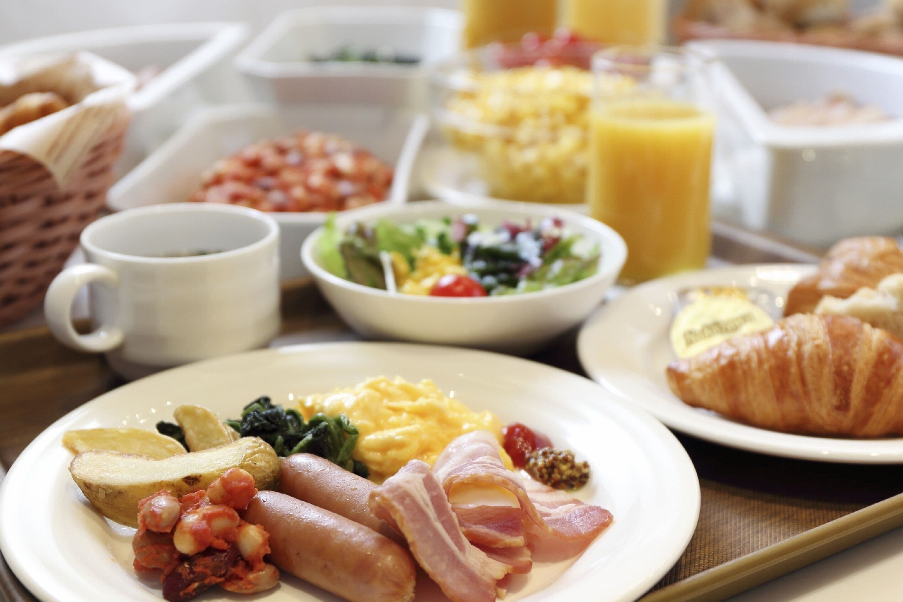 Un bufé de desayuno con diversos platos, incluyendo huevos, tocino, papas y un croissant.