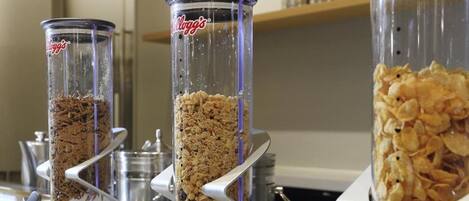 A breakfast buffet with various food items in dispensers, including cereal and granola.