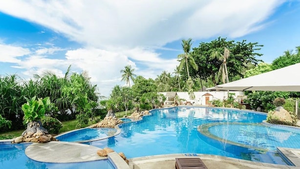 Ein Pool mit geschwungenem Design, umgeben von tropischer Vegetation und blauem Himmel.