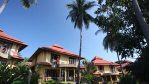 Ein mehrstöckiges Hotel mit roten Dächern und Balkonen, umgeben von üppiger Vegetation und Palmen.
