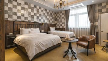 Quarto de hotel com duas camas, um candelabro, cabeceira de madeira, uma mesa redonda, uma poltrona de couro e parede xadrez.