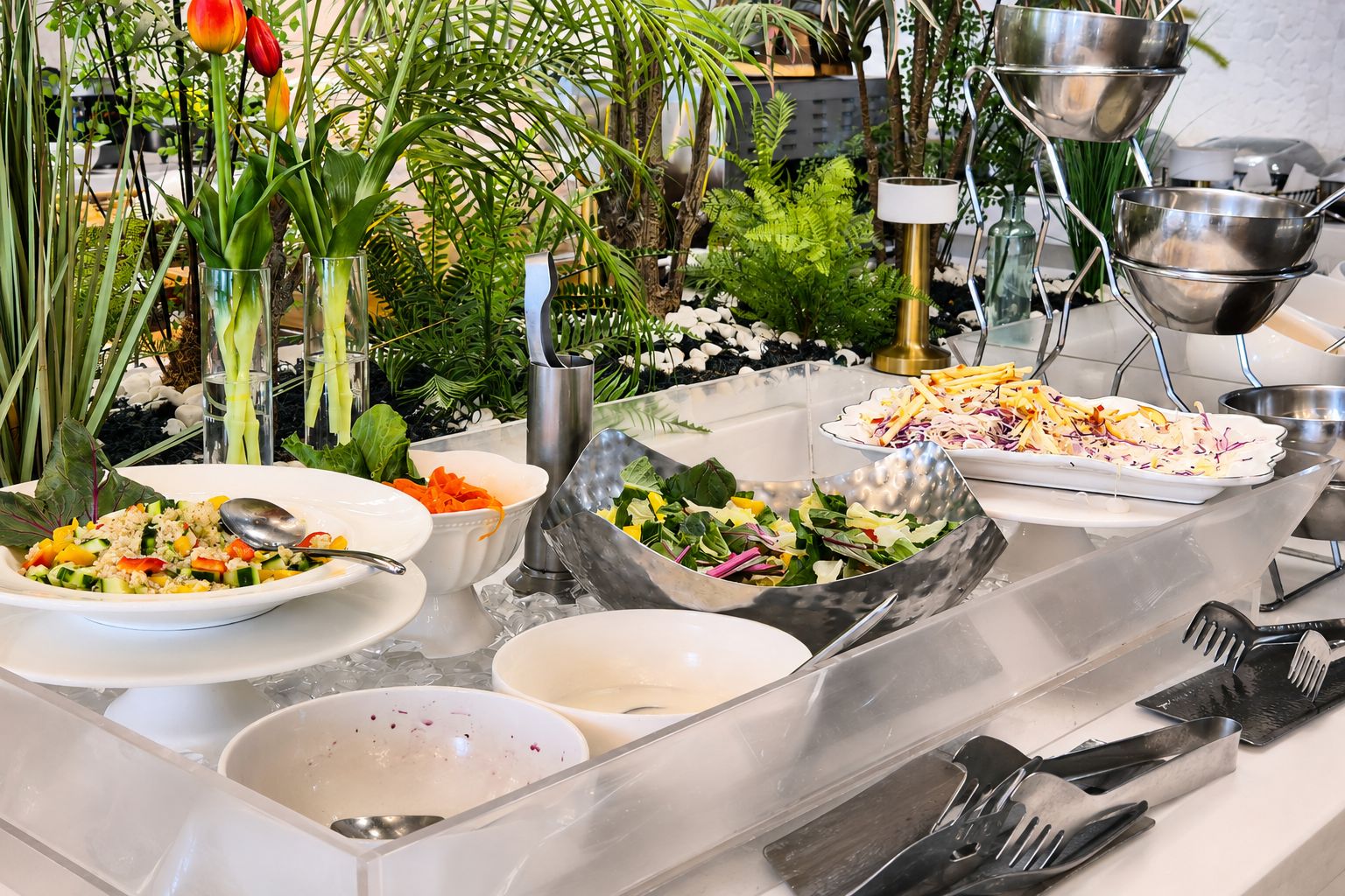 A buffet setup with various dishes, including salads and a vegetable dish, arranged on a table with clear glassware and metal serving dishes.