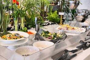 A buffet setup with various dishes, including salads and a vegetable dish, arranged on a table with clear glassware and metal serving dishes.
