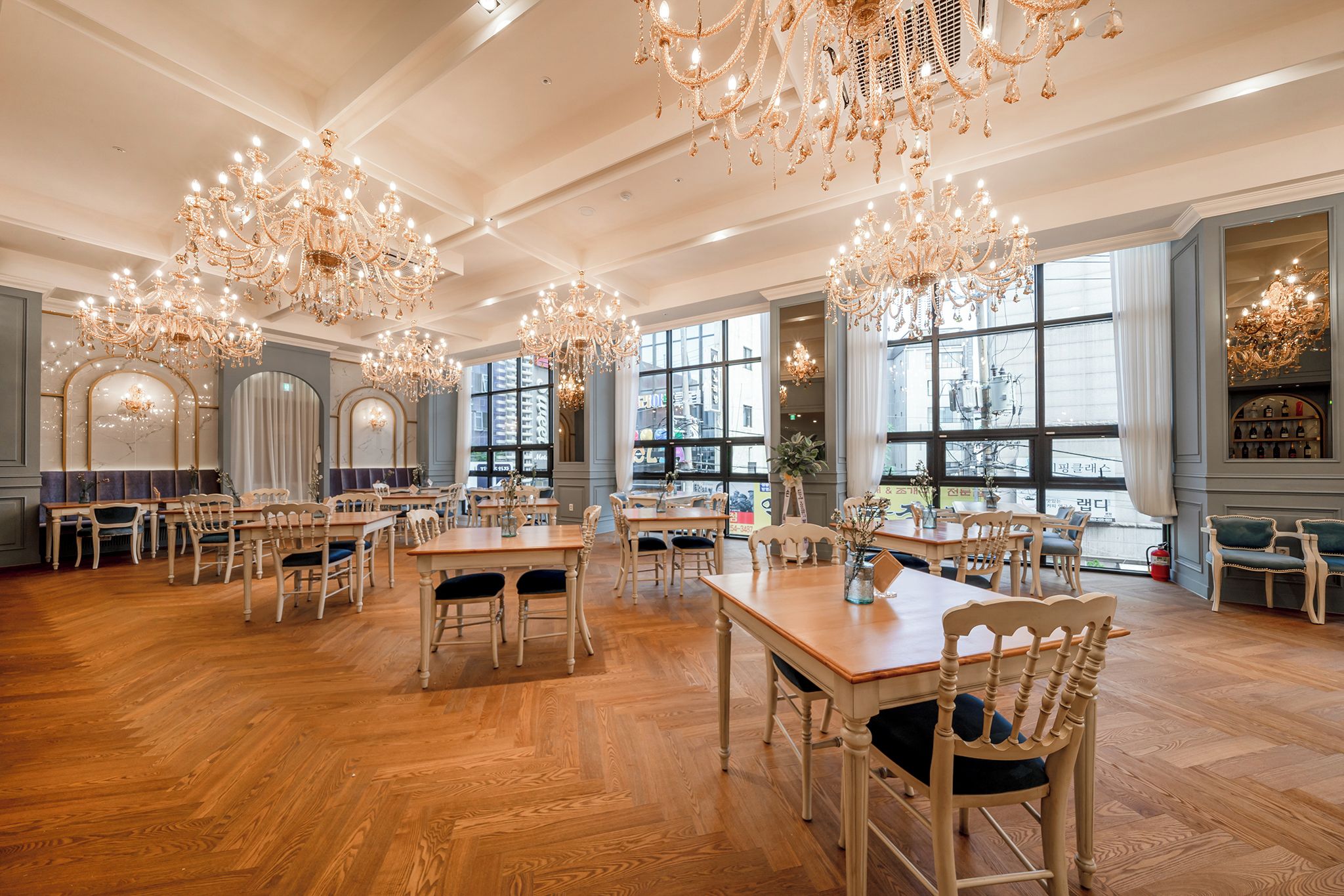 A spacious dining area with multiple tables and chairs, large windows, and ornate chandeliers.