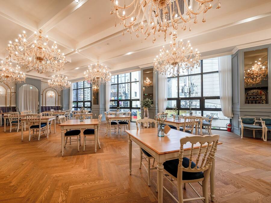 A spacious dining area with multiple tables and chairs, large windows, and ornate chandeliers.