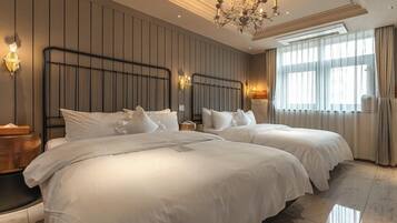 Habitación de hotel con dos camas, un candelabro, un ventanal con cortinas y una lámpara fijada a la pared.