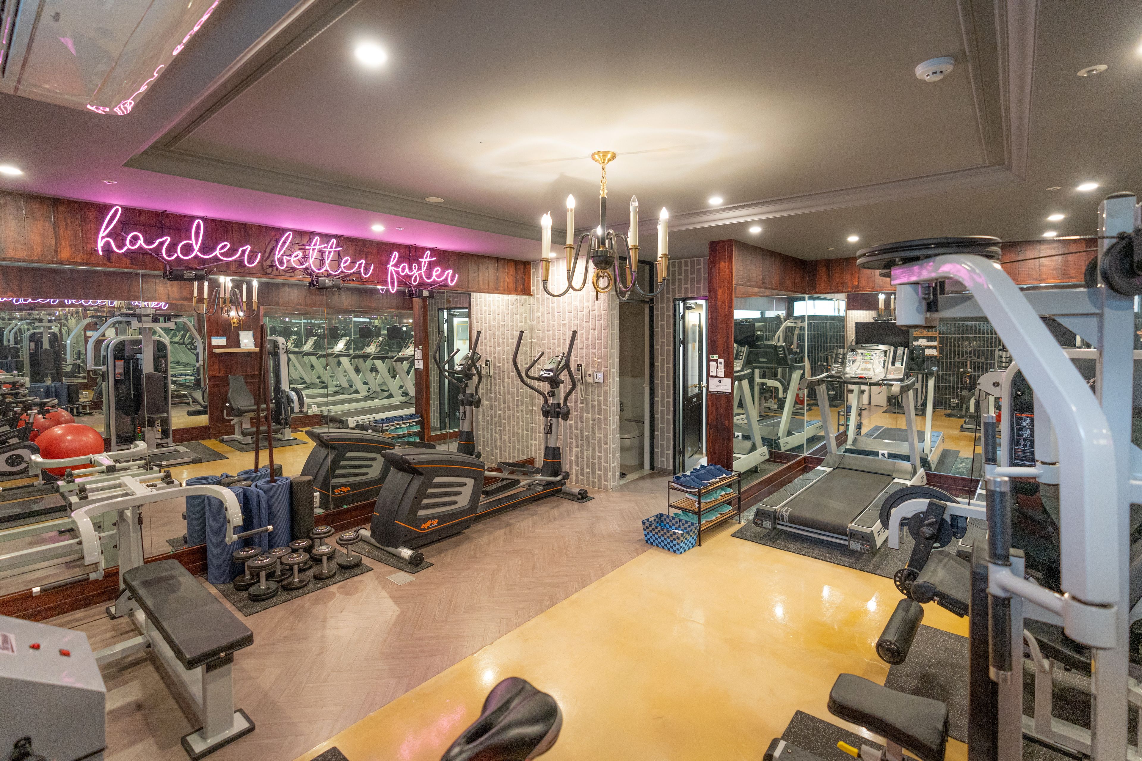 Un gimnasio con diversos equipos de ejercicio, un letrero de neón y un espejo que refleja el espacio.