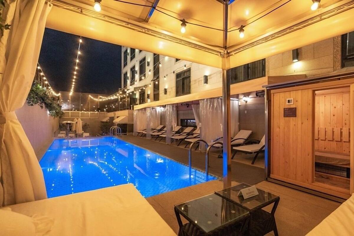 Uma área de piscina com espreguiçadeiras, uma mesa de vidro e uma sauna.