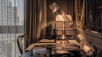 A room with a desk, a lamp, a record player, and a window with curtains.