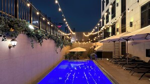 Un espace piscine aménagé pour la nuit, avec des guirlandes lumineuses, des chaises longues et des parasols.