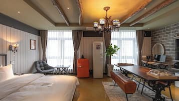 Hotellihuone, jossa on sänky, työpöytä, tuoli, penkki, televisio, peili ja kattokruunu.