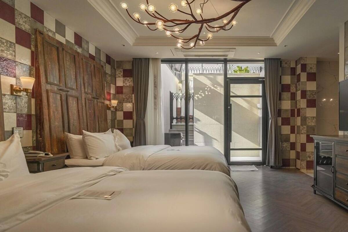 Quarto de hotel com duas camas, televisão, candelabro e vista para uma escadaria.