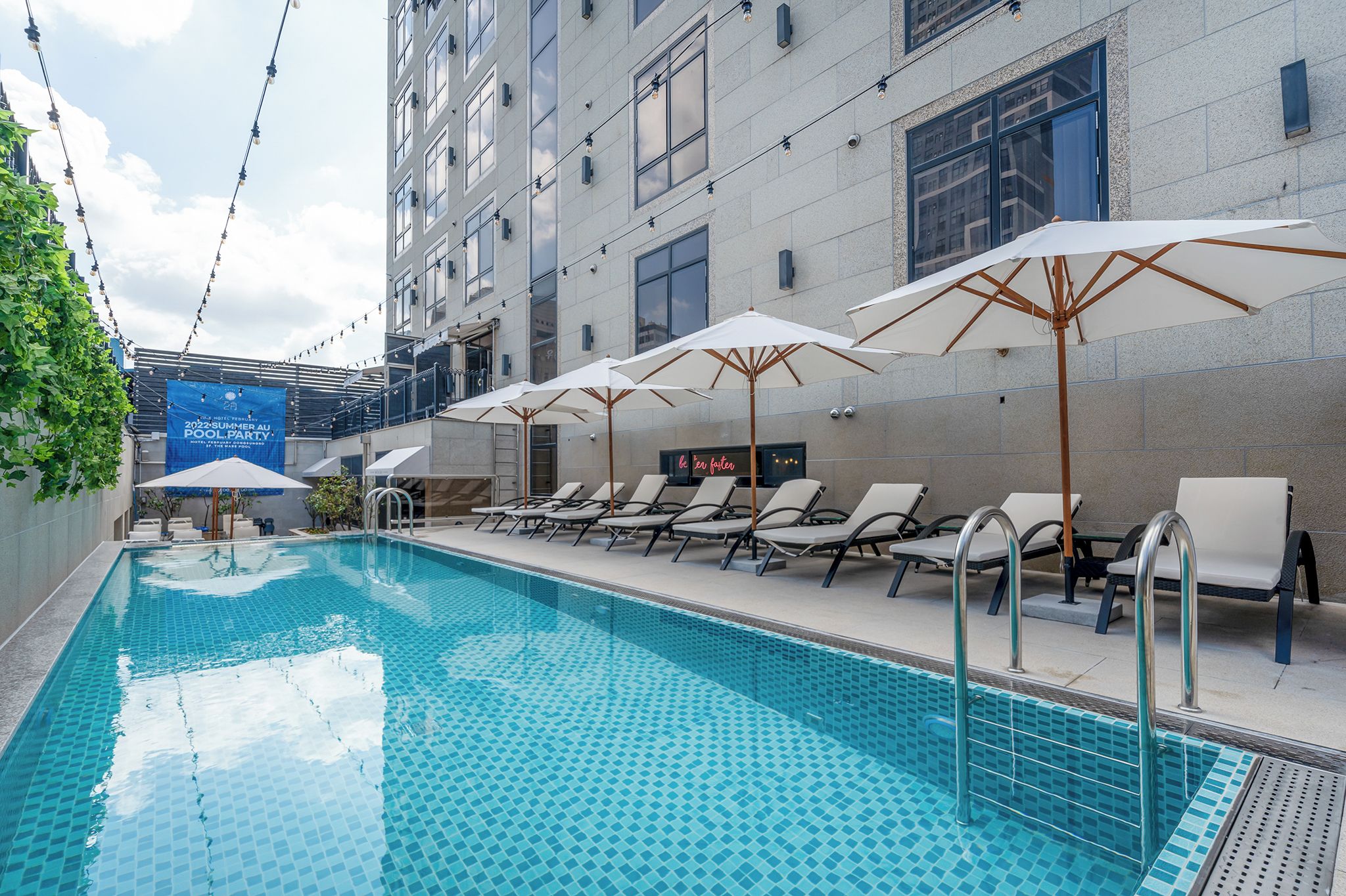 A swimming pool with lounge chairs and umbrellas, a building with a sign, and a clear sky.