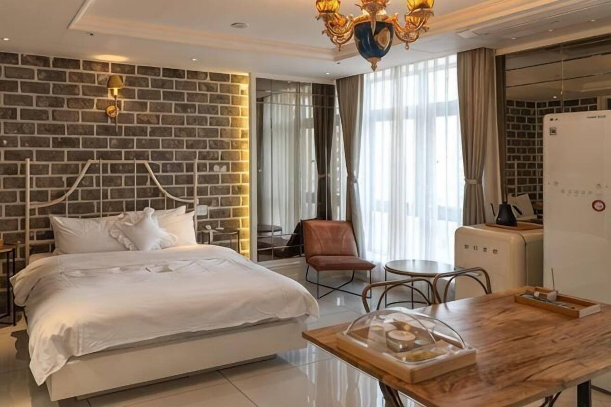 A hotel room with a brick-patterned wall, a bed, a dining table, and a chair.