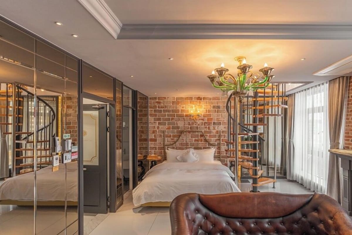 A bedroom with a bed, a chandelier, a brick wall, and a staircase.