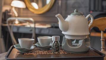 A teapot and cups on a tray with a woven mat, a small bottle, and a mirror in the background.