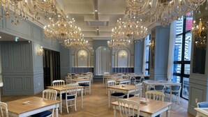 Un vaste espace dédié à la salle à manger, avec de nombreuses tables et chaises, de magnifiques lustres et de grandes fenêtres laissant entrer la lumière naturelle.