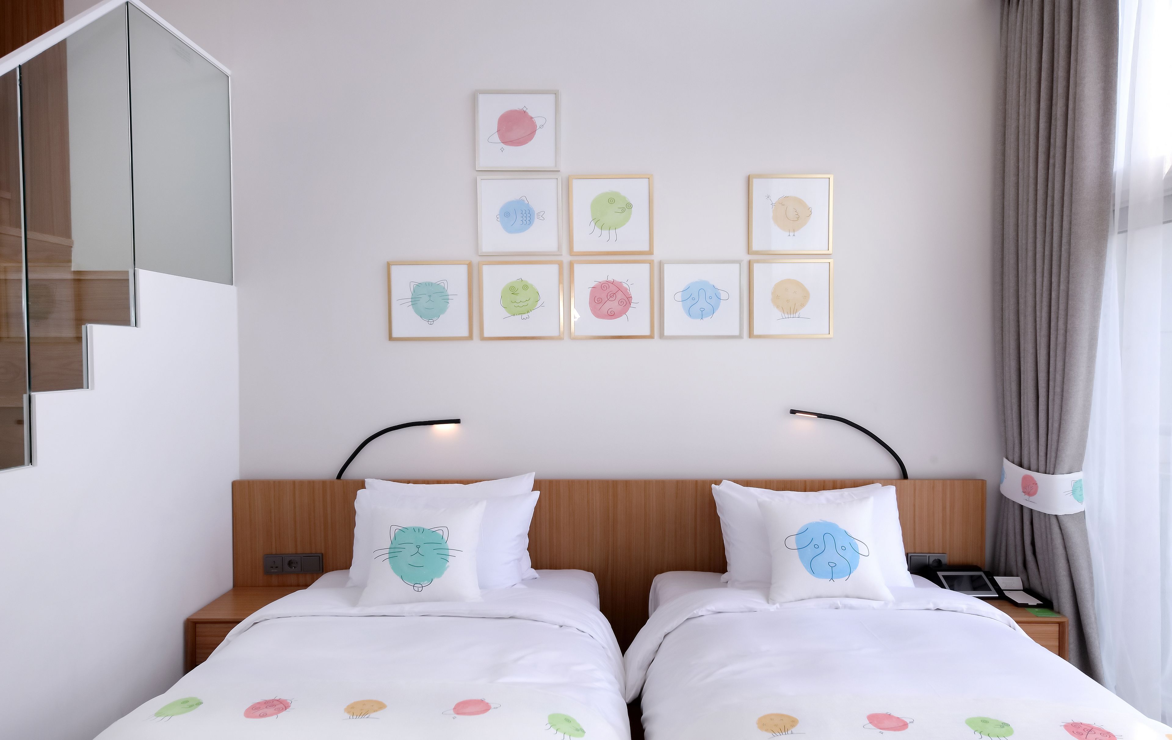 A hotel room with two beds, a staircase, and a wall with framed artwork.