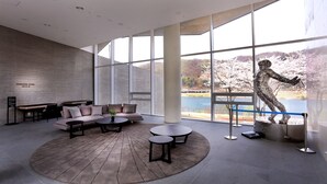 A spacious lounge area with a large window offering a view of a lake and cherry blossoms. - Midas Hotel & Resort (Gapyeong)
