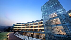 A modern hotel with a glass facade, multiple floors, and a wooden deck with lights. - Midas Hotel & Resort (Gapyeong)