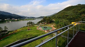 A scenic view of a park with a lake, a bridge, and mountains in the background. - Midas Hotel & Resort (Gapyeong)