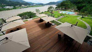A deck with outdoor seating and umbrellas overlooking a river and mountains. - Midas Hotel & Resort (Gapyeong)