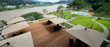 A deck with outdoor seating and umbrellas overlooking a river and mountains.