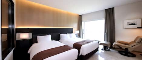 A hotel room with two beds, a sofa, a chair, a large window, and a framed picture on the wall.