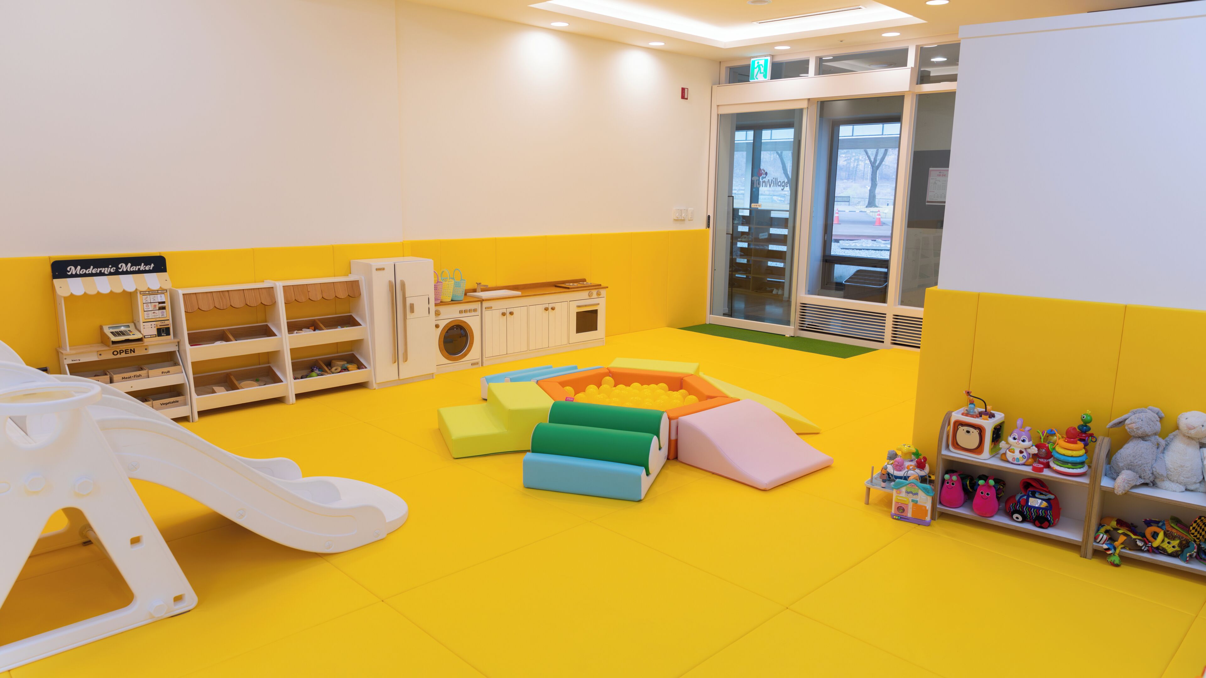 Un área de juegos infantil, muy colorida, con un tobogán, colchonetas y estanterías.