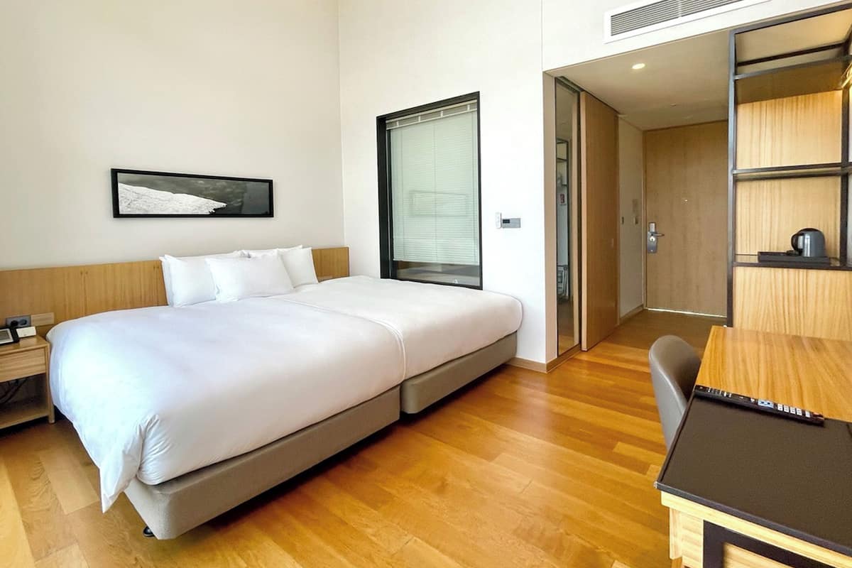 A modern hotel room with a bed, bedside table, and a desk with a chair.