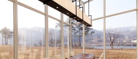 A conference room with a long table, chairs, and large windows offering a view of a landscape with trees and mountains.