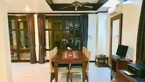 Un coin repas avec une table et des chaises, un ventilateur de plafond, un téléviseur posé sur un meuble et une porte-fenêtre coulissante donnant sur un balcon.