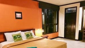 Une chambre d’hôtel avec un mur orange, un lit recouvert d’une couverture beige, deux oreillers, une table de chevet avec une lampe et une fenêtre donnant sur l’extérieur.