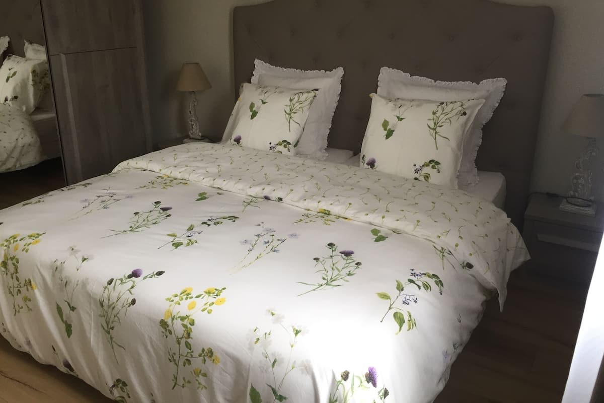 A neatly made bed with floral bedding and two pillows, a bedside lamp, and a small statue on a nightstand.