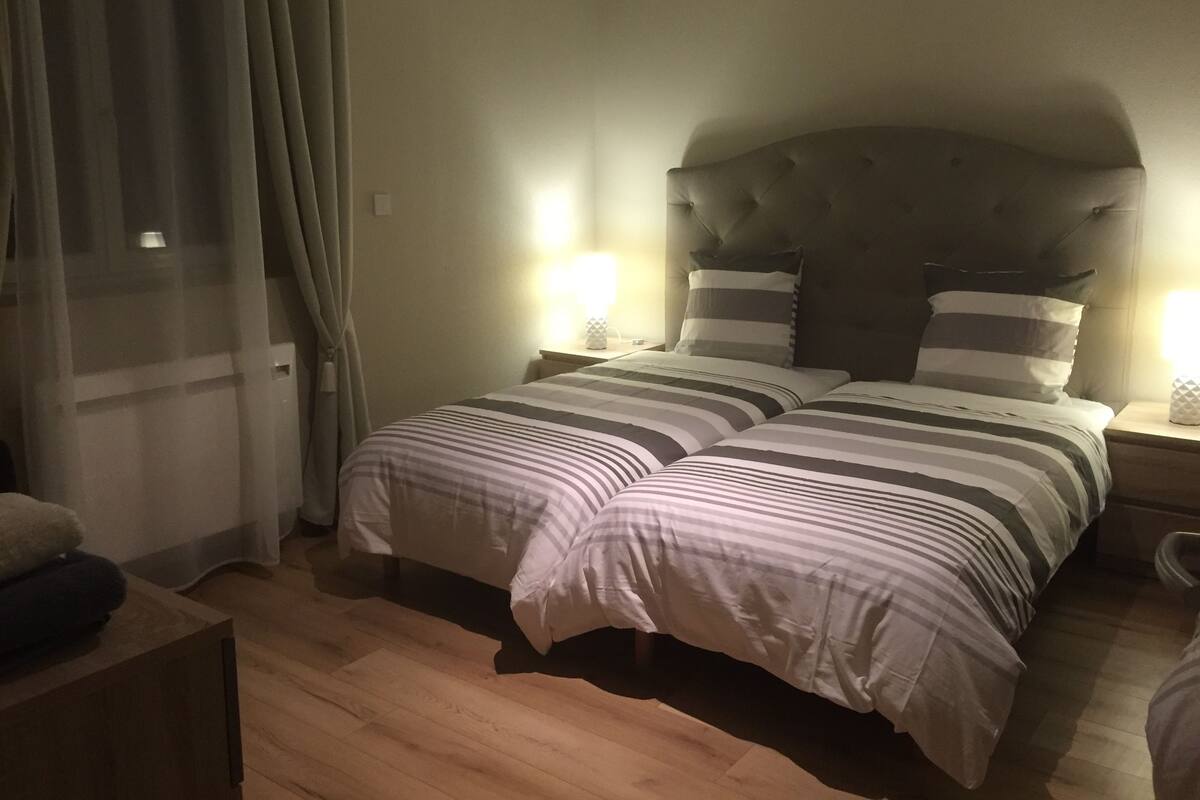 A double bed with striped bedding, a tufted headboard, bedside lamps, and a wooden floor.