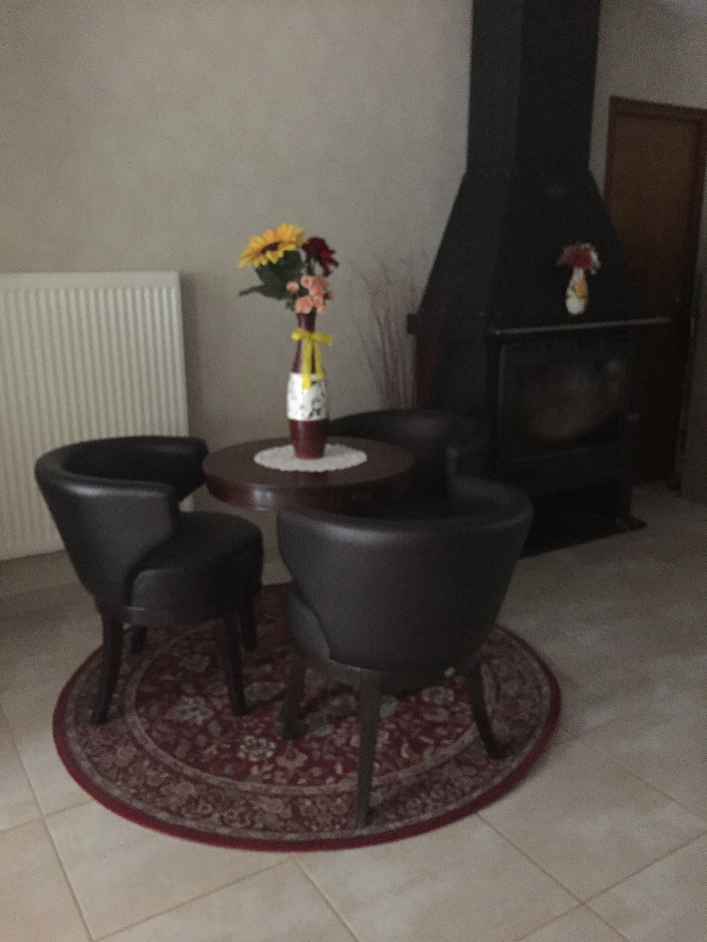A living room with a fireplace, a round table with chairs, and a decorative vase with flowers.