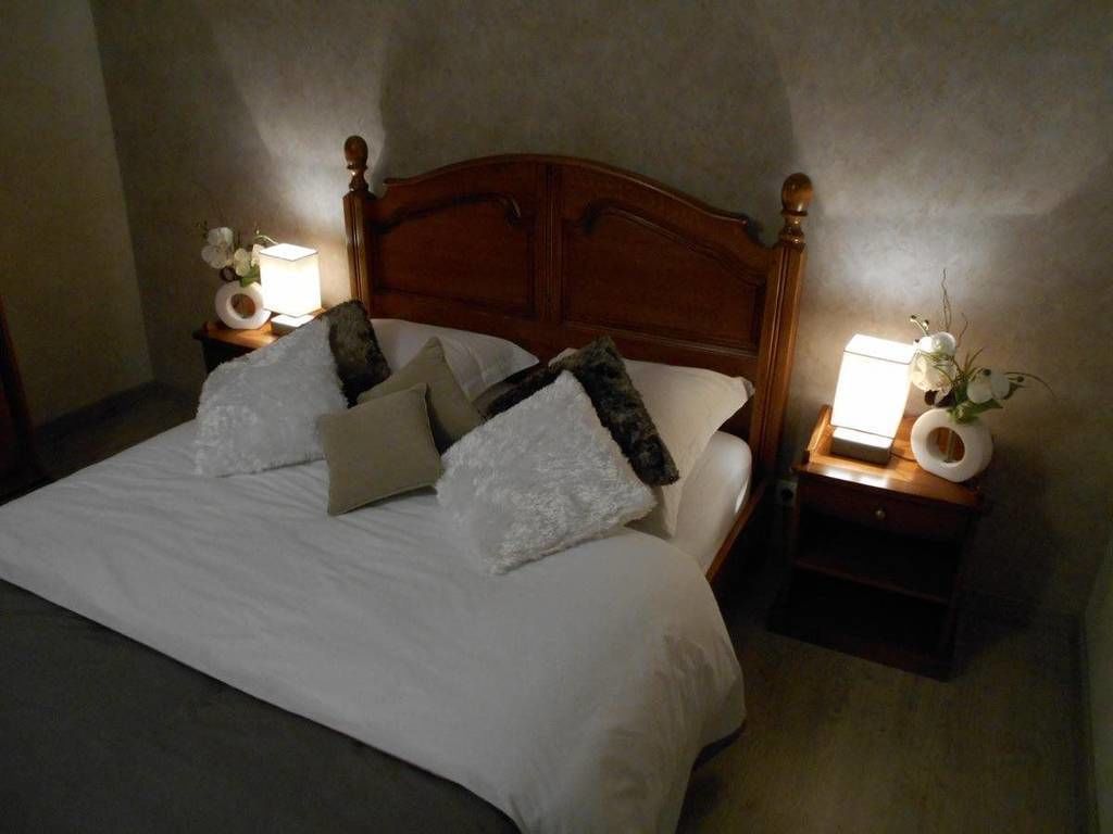 A neatly made bed with white linens and multiple pillows, flanked by wooden nightstands with lamps and small vases.