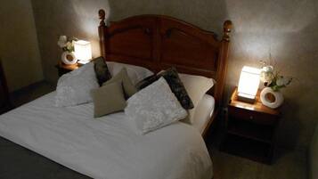 A neatly made bed with white linens and multiple pillows, flanked by wooden nightstands with lamps and small vases.