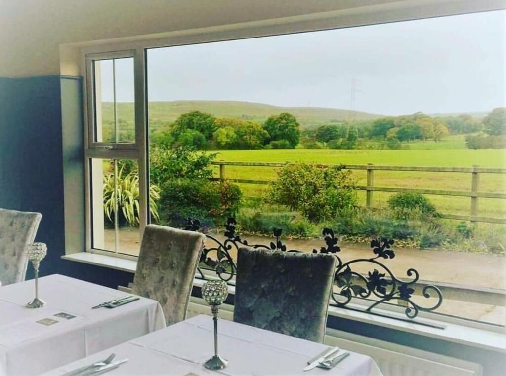 A dining area with tables set for two, a view of a green landscape through large windows.
