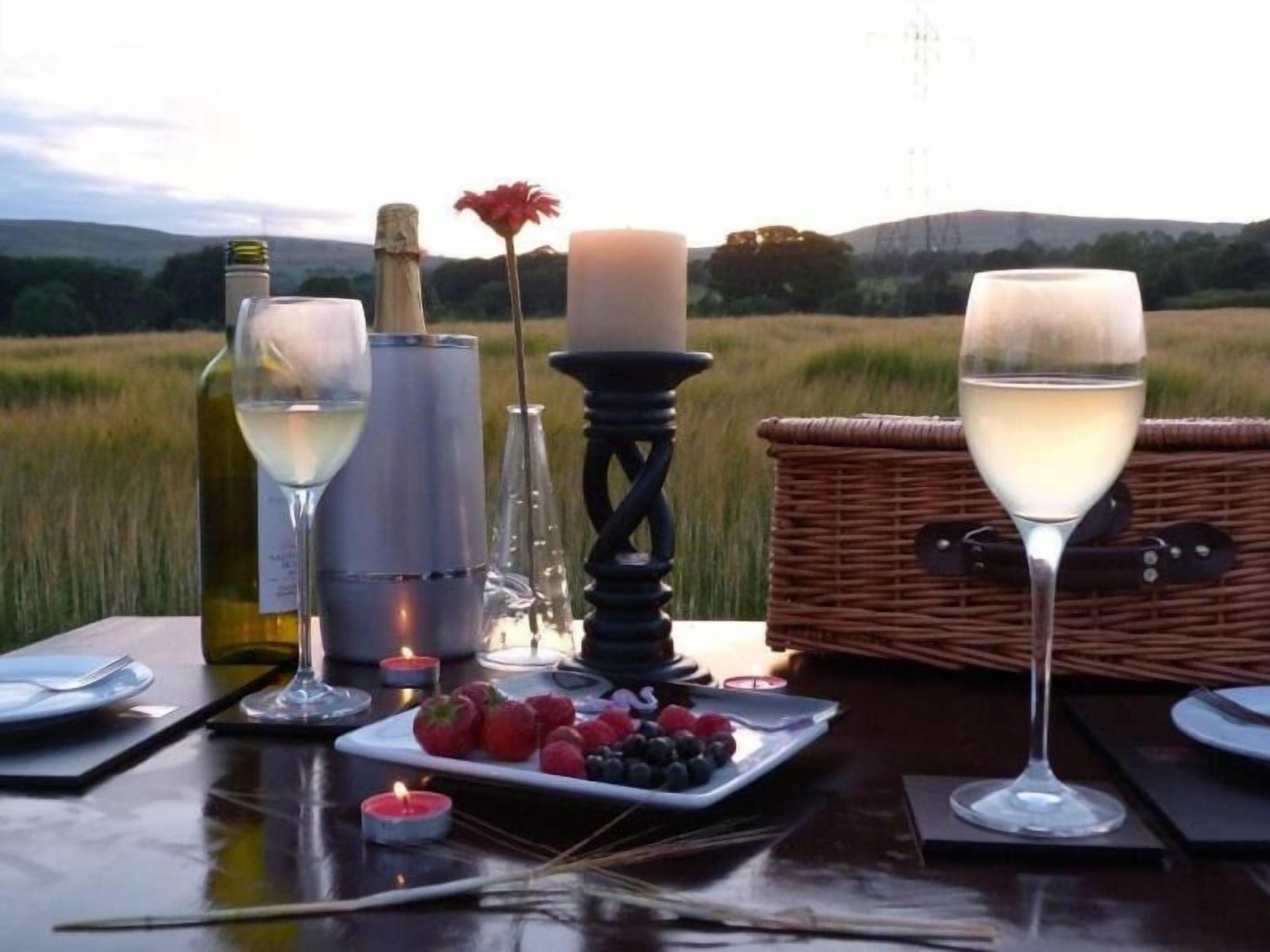 Mesa lista para una comida, con copas de vino, una vela y una cesta de fruta.