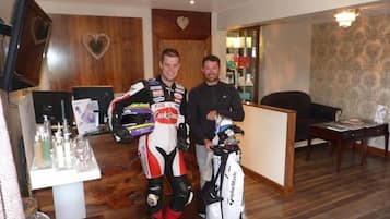 A room with a wooden reception desk, a television mounted on the wall, and a table with various items including a golf bag.