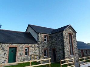 A stone building with a green door, a large window, and a wooden fence. - Dunamoy Cottages & Spa (Ballyclare)