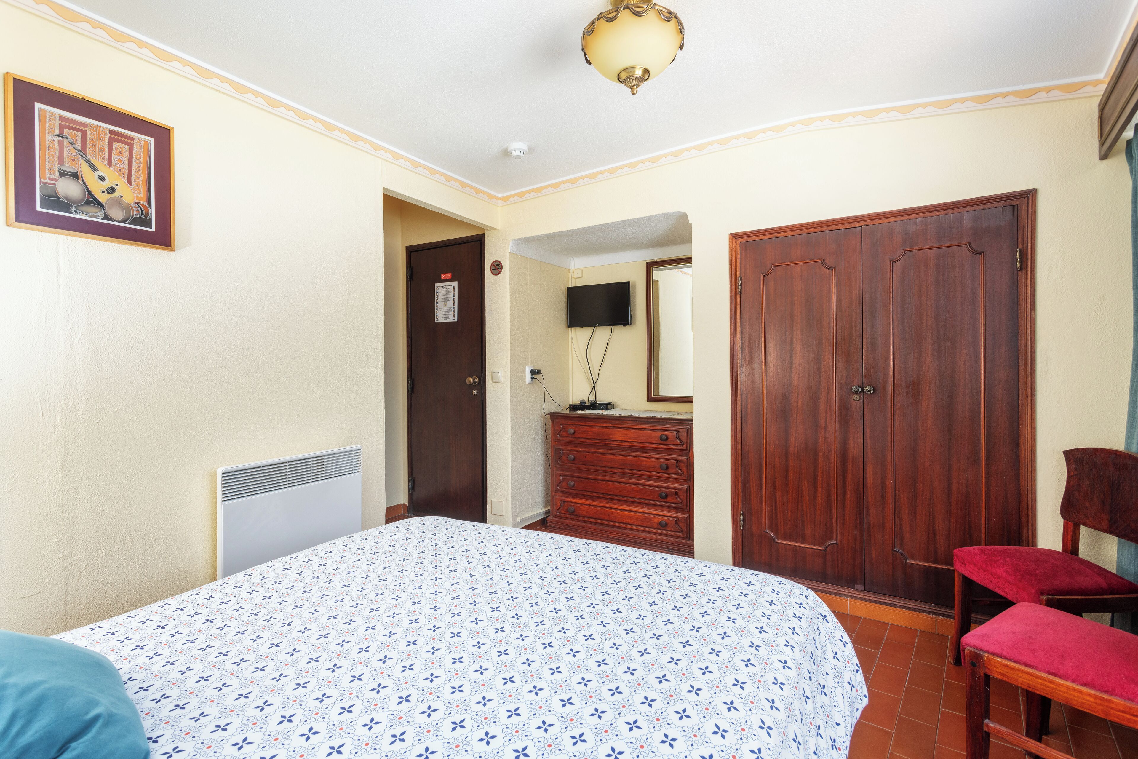 A bedroom with a bed, a dresser, a television, and a wardrobe.